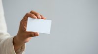 Hand holding blank white business card against neutral background, suitable for branding, corporate identity, and marketing mockup designs.
