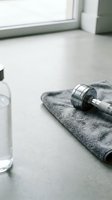 Chrome dumbbell resting on gray towel next to water bottle and window, fitness equipment for strength training and home gym workouts.