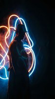 Young man silhouette with colorful neon light trails creating artistic patterns in dark studio environment for creative projects and modern design concepts.