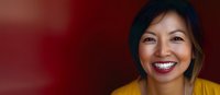 Asian woman in yellow sweater with bright genuine smile against dark red background, horizontal banner format for business and lifestyle marketing content.