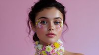 Young Asian woman with creative floral makeup and fresh flower necklace against pink background, showcasing spring beauty and artistic cosmetic application.