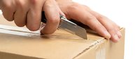 Hands using utility knife to open cardboard box, isolated on white background for packaging and shipping design use.