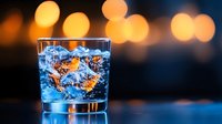 Refreshing cocktail with ice cubes and golden bokeh lights in background, suitable for beverage, bar, and hospitality marketing materials.