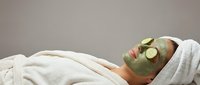 Woman relaxing with green clay facial mask and cucumber slices on eyes during spa treatment. Professional skincare and wellness therapy session.