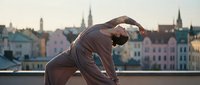 Man in brown athletic wear performing side stretch exercise outdoors with historic waterfront cityscape and colorful buildings in background during golden hour.