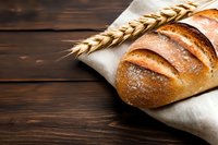 Fresh crusty bread loaf with golden crust and wheat ear on rustic wooden background with white linen napkin, close up view of artisanal baking.