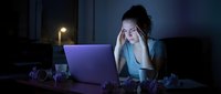 Young African American businesswoman experiencing stress and fatigue while working late at night on laptop computer in dark office environment.