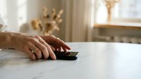 Close-up of a woman's hand with rings using a smartphone on a marble table in a bright modern interior.