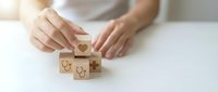 Woman arranging wooden blocks with healthcare symbols including heart and stethoscope icons on white surface for medical insurance concept.