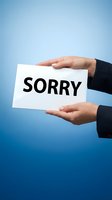 Businesswoman in dark suit holding white card with word Sorry on blue background, expressing apology and regret in professional setting.