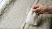 Senior adult hand holding white tea bag over natural linen fabric background for beverage, wellness, and lifestyle content.