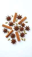 Aromatic spices arranged in circular pattern with cinnamon sticks, star anise and cardamom pods on white background for culinary and cooking projects.