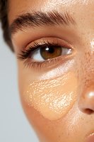 Close-up of brown eye with long eyelashes and glowing dewy skin showing natural makeup and highlighting effects on mixed race female model's face.