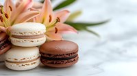 French macarons in vanilla and chocolate flavors stacked elegantly beside pink lily flowers on white marble surface, creating luxurious dessert composition.