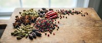 Aromatic spices and peppercorns scattered on rustic wooden cutting board in bright kitchen. Culinary ingredients for cooking and seasoning dishes.