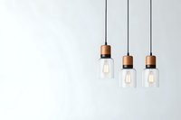 Modern pendant lights with copper fittings and clear glass shades hanging against white wall, featuring warm glowing Edison bulbs creating minimalist interior design.