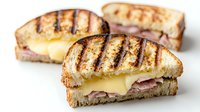 Grilled sandwich with melted cheese and ham on toasted white bread, featuring golden-brown grill marks and oozing yellow cheese, photographed on white background for menu design.