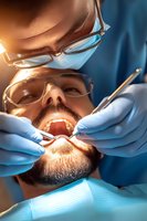 Male patient receiving dental treatment from professional dentist wearing protective equipment. Close-up view of dental procedure in modern clinic.
