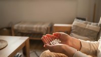 Person holding white pills or medication tablets in cupped hands in cozy living room setting for healthcare and wellness concepts.