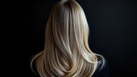 Back view of long blonde straight hair on dark background, highlighting natural movement and shine. Professional hairstyling and beauty concept.