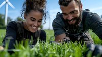 Young mixed race woman and bearded Middle Eastern man in black clothing examining grass near wind turbine, environmental scientists studying sustainable agriculture.