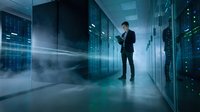 Professional businessman in suit working with tablet in modern data center server room with blue lighting and digital network effects.