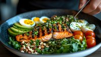 Grilled salmon fillet with herb crust served on fresh greens, avocado slices, boiled eggs and cherry tomatoes in black bowl for healthy dining.