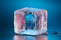 Melting ice cube with pink and blue color reflection on dark background, water drops and dramatic lighting create atmospheric composition.