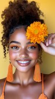Young African American woman with curly hair holding orange gerbera flower against yellow background. Natural beauty portrait with tassel earrings and bright smile.