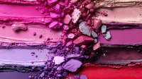 Crushed makeup powder swatches in vibrant pink, purple and red shades with scattered particles creating artistic texture on flat surface. Cosmetic product photography.