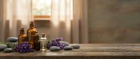 Spa wellness setup with essential oil bottles, lavender flowers and smooth stones on wooden surface in natural sunlight for relaxation therapy.