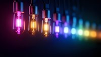 Colorful vintage Edison bulbs hanging in row with glowing filaments creating rainbow spectrum lighting effect against dark background for creative projects.
