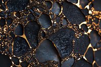 Black stones with golden light shining through cracks create dramatic abstract pattern. Textured dark rocks illuminated by warm glowing highlights form artistic composition.