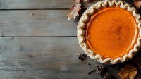 Fresh homemade pumpkin pie with flaky crust on rustic wooden background decorated with autumn leaves and star anise spices, overhead view with copy space.