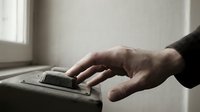 Male hand with pale skin tone pressing a doorbell button on a modern intercom system mounted on a wall, suitable for home security, access control, and residential entry concepts.