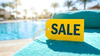 Yellow sale tag on turquoise towel by sunny resort pool, promoting summer discounts, travel deals, and seasonal retail promotions.