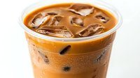 Refreshing iced coffee drink with milk in plastic cup, condensation droplets on surface, ice cubes floating in creamy brown liquid against white background.
