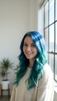 Young woman with vibrant blue and teal ombre hair smiling in bright modern interior with large windows wearing cozy beige sweater for lifestyle content.