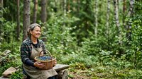 Mature woman forager in forest holding wicker basket filled with mushrooms, surrounded by green trees and woodland vegetation for nature and outdoor lifestyle content.