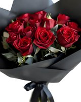 Elegant bouquet of fresh red roses wrapped in black matte paper with satin ribbon, romantic floral arrangement for Valentine's Day or anniversary celebration.