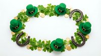 St. Patrick's Day decorative frame with green leprechaun hats, shamrock leaves, gold coins and horseshoes arranged in oval border on white background for holiday celebrations.
