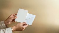 Woman holding blank white envelope and card against neutral beige background for stationery, correspondence, invitation, or greeting card mockup projects.