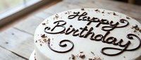 Decorated cake with chocolate script lettering reading Happy Birthday, topped with cocoa crumbles and swirled frosting details on wooden surface for celebration events.
