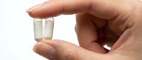 Hand holding two white capsule pills between fingers on clean background for healthcare and pharmaceutical concepts.