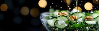 Fresh green salad with cherry tomatoes and herbs in glass bowl with sparkling water droplets against festive bokeh lights background for healthy dining.