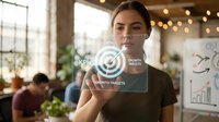 Young Hispanic businesswoman touching holographic KPI dashboard interface in modern office with string lights and coworkers in background.
