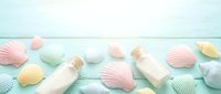 Pastel colored seashells and bottles scattered on light blue wooden background. Summer beach vacation concept with soft mint, pink, yellow shell collection.