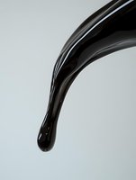 Thick black liquid pouring in elegant curved stream against light background, creating dramatic contrast and glossy reflection for cosmetic or food design.