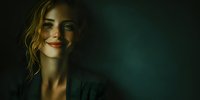 Young woman with wavy hair smiling mysteriously in dramatic lighting against dark background for portrait photography and creative projects.