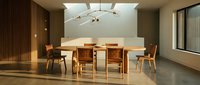 Modern dining room with wooden table and chairs under skylight, featuring minimalist interior design with concrete flooring and neutral tones for contemporary home decor.